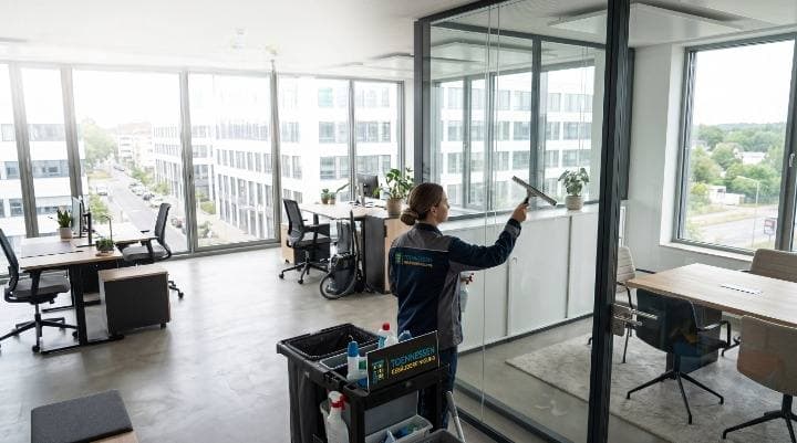 Büroreinigung Neuss – Toennessen Mitarbeiterin reinigt Glastrennwand im Großraumbüro